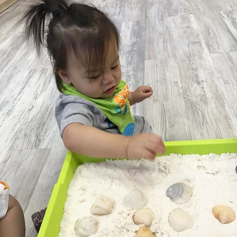 A little girl is playing with sand and rocks in a green tray