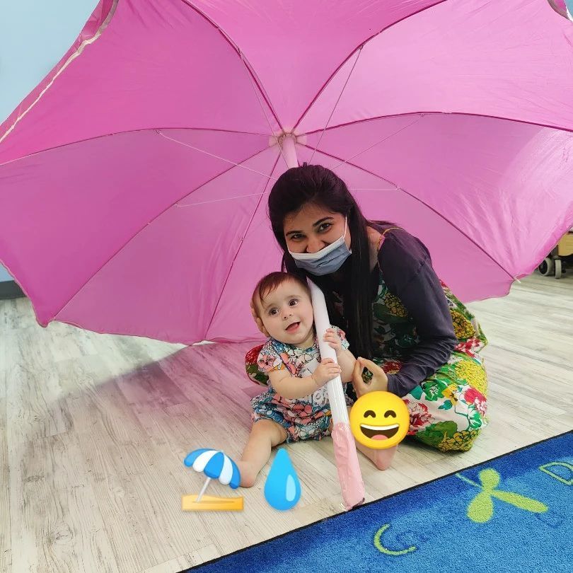 A woman and a baby are sitting under a pink umbrella