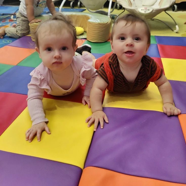 Two babies are crawling on a colorful mat