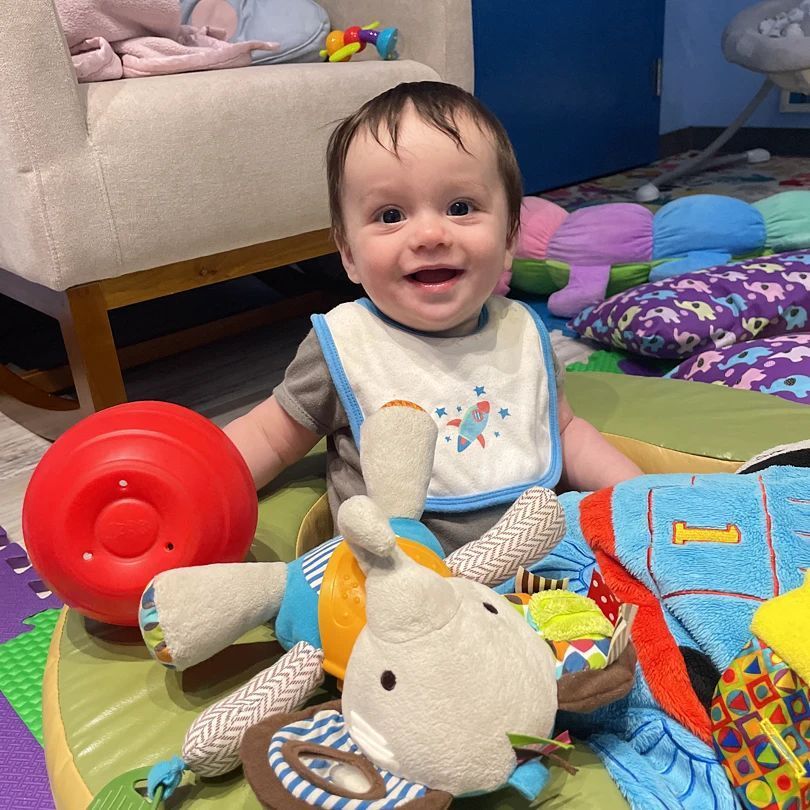 A baby wearing a bib is sitting on the floor with stuffed animals