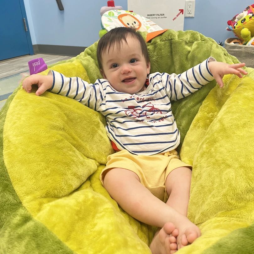 A baby is sitting in a bean bag chair with his arms outstretched