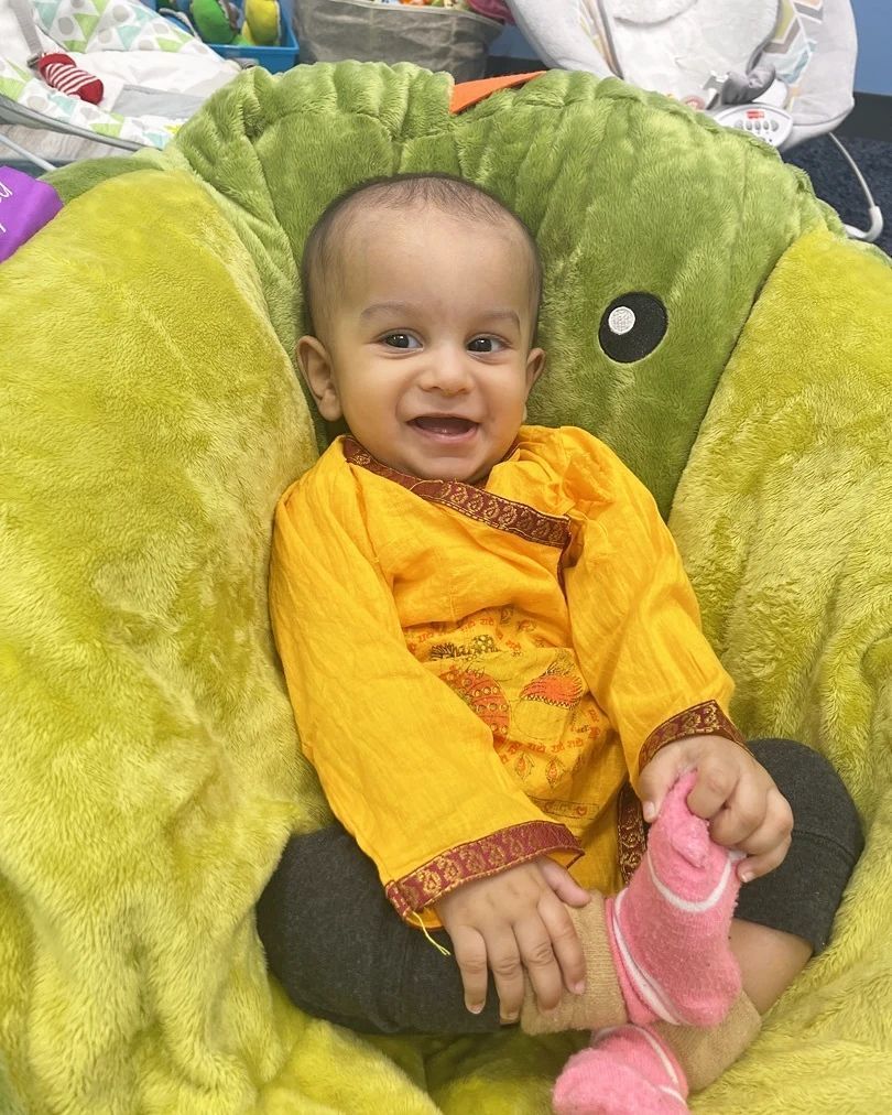A baby is sitting in a green chair wearing pink socks