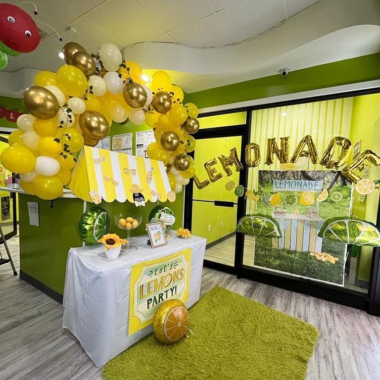 A room decorated for a lemonade party with balloons and a lemonade stand