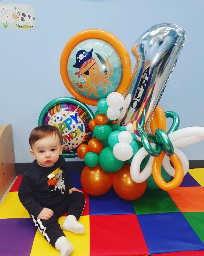 A baby is sitting in front of a number one balloon