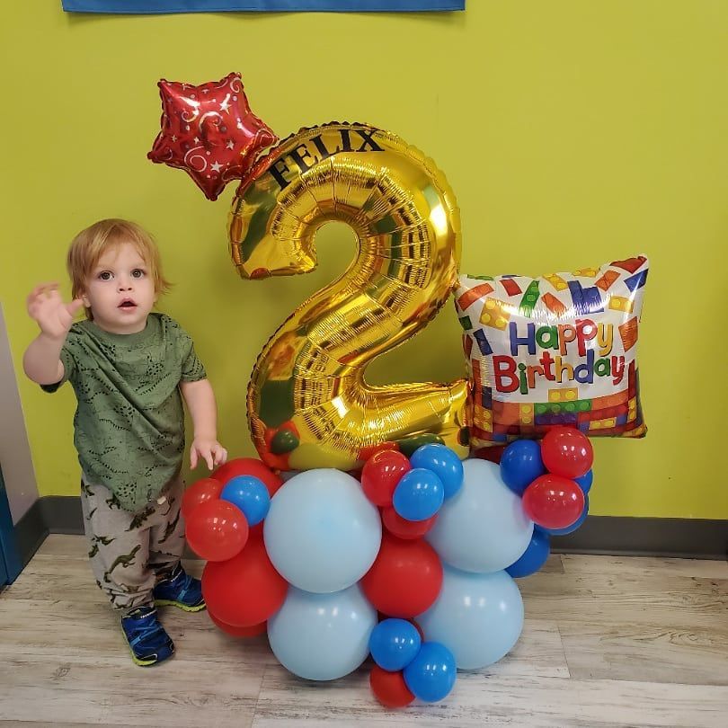 A little boy is standing next to a balloon that says felix on it