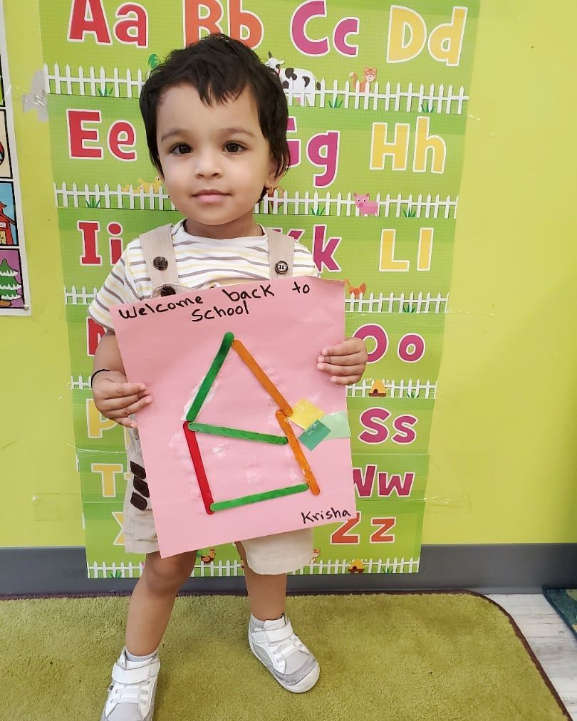 A little girl is holding a piece of paper with a triangle on it
