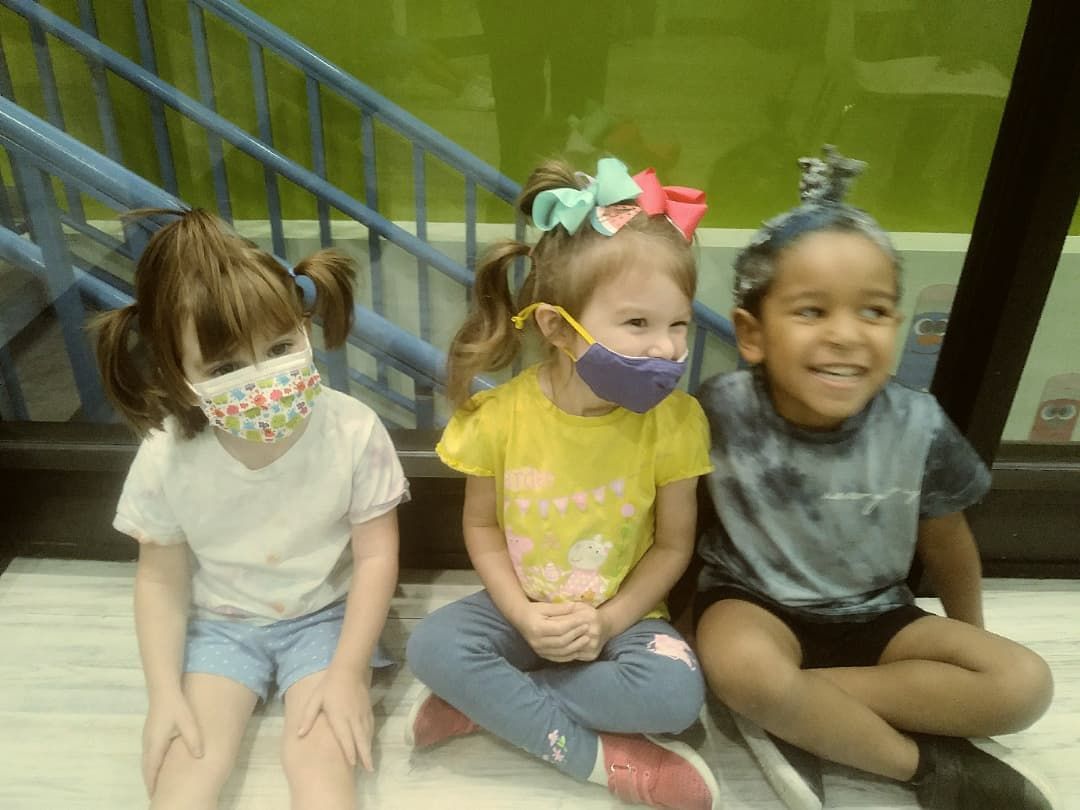 Three little girls wearing face masks are sitting on the floor