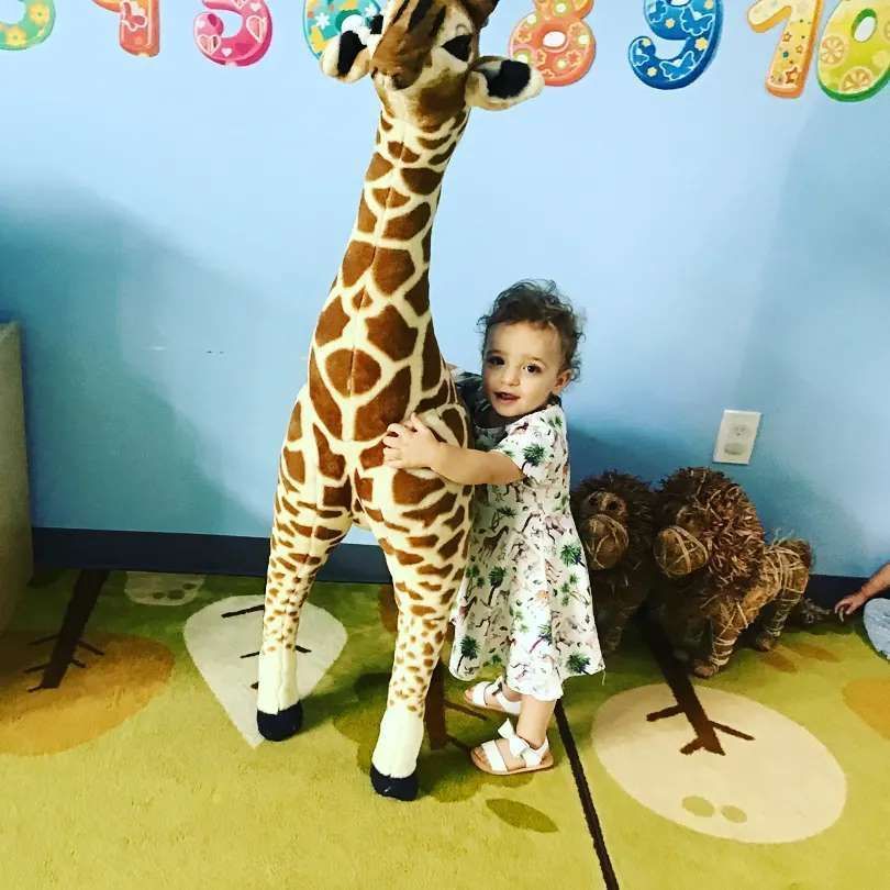 A little girl is hugging a stuffed giraffe