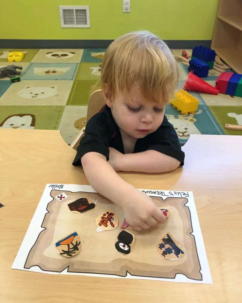 A little boy is sitting at a table playing with a treasure map