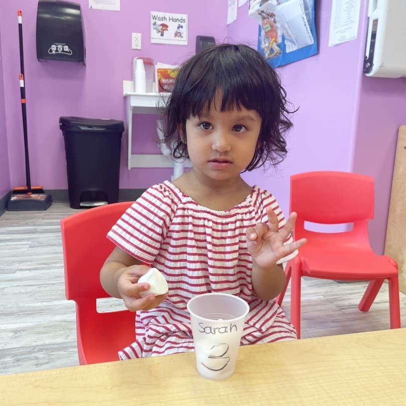 A little girl is sitting at a table with a cup that says sarah on it