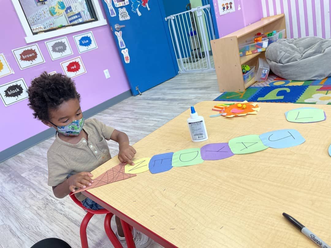 A young boy wearing a mask is sitting at a table in a classroom