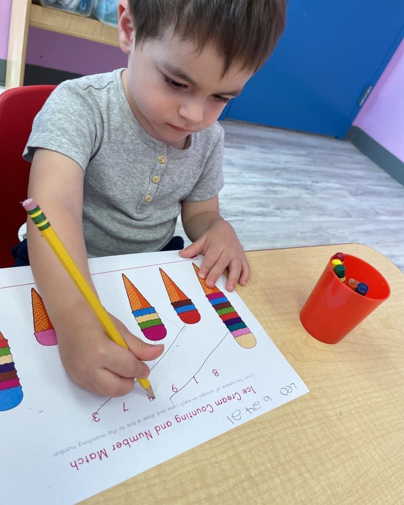 A young boy is drawing ice cream cones on a piece of paper