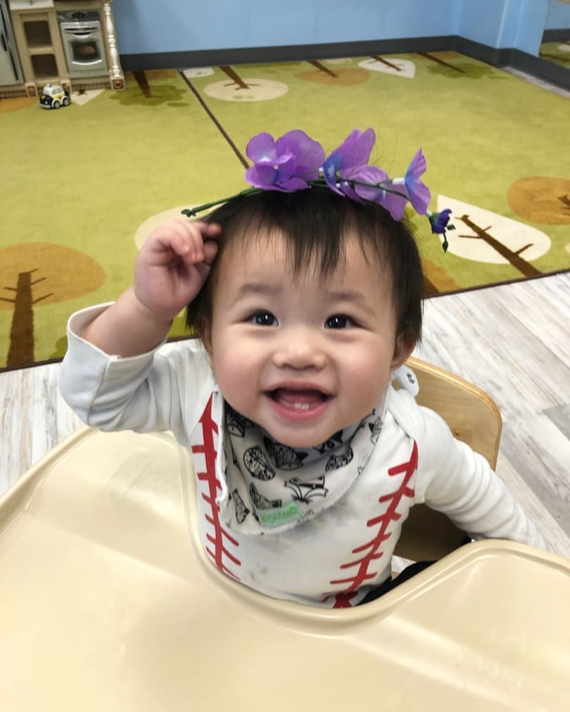 A baby wearing a purple flower headband is sitting in a high chair