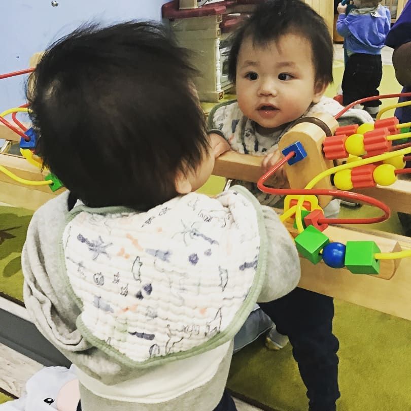 A baby playing with a toy in front of a mirror