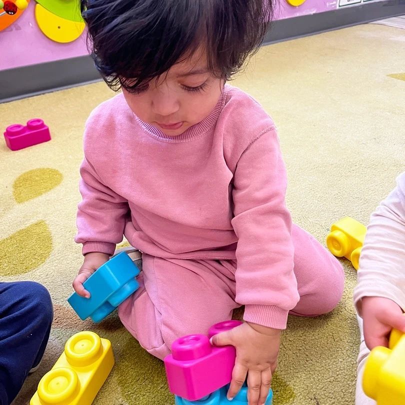 A little girl in a pink sweater is playing with toy blocks