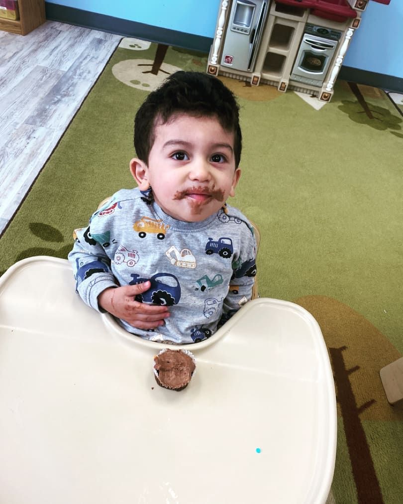 A little boy is sitting in a high chair eating a cupcake