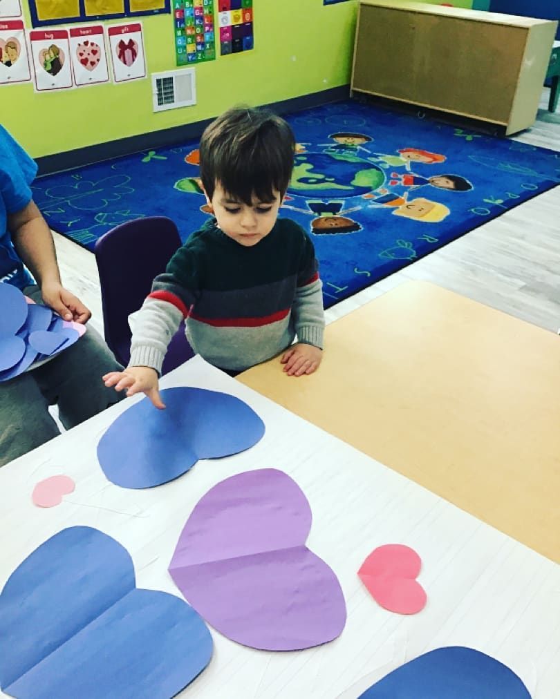 A little boy is sitting at a table with paper hearts on it