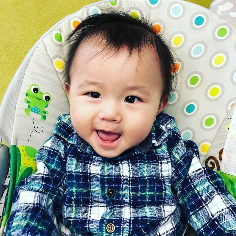 A baby in a plaid shirt is sitting in a high chair
