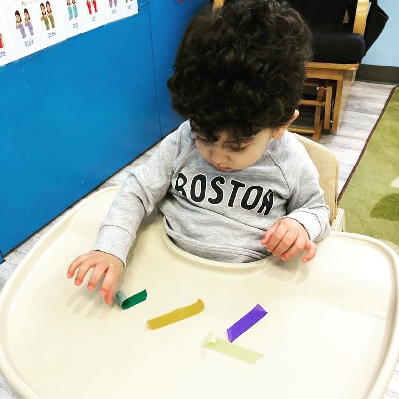 A baby wearing a boston shirt is sitting in a high chair