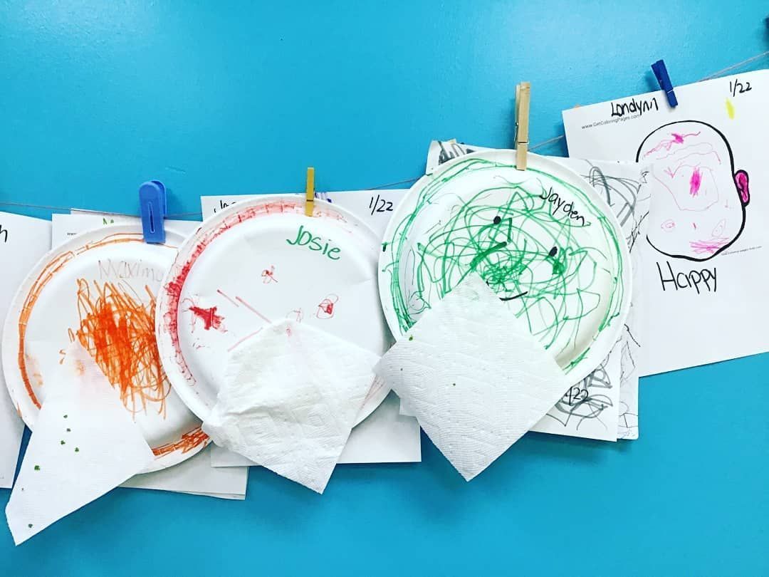 A row of paper plates with drawings on them hanging on a blue wall