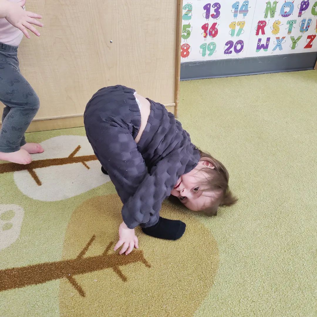 A child is crawling on the floor in front of a wall with the alphabet on it