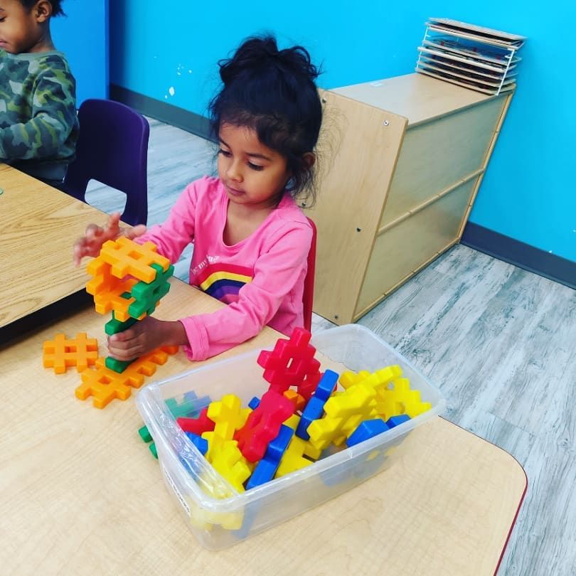 A little girl in a pink shirt is playing with plastic blocks