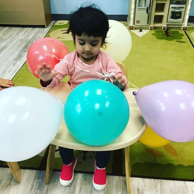 A little girl is sitting at a table playing with balloons