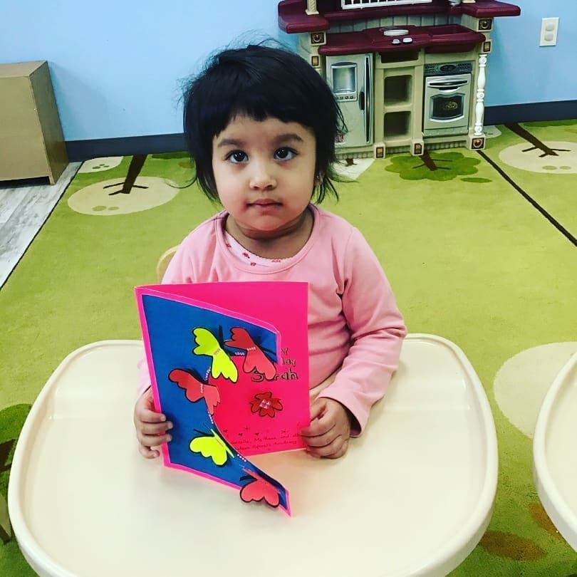 A little girl is sitting at a table holding a card with butterflies on it