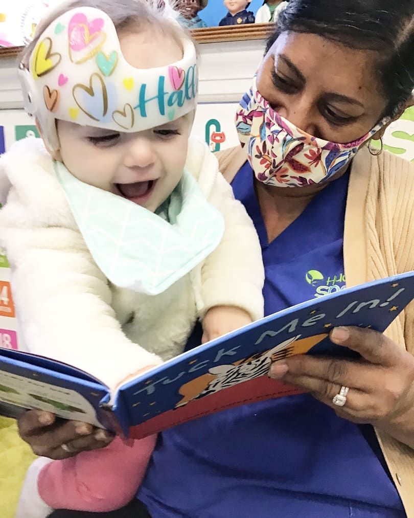 A woman wearing a mask is reading a book to a baby