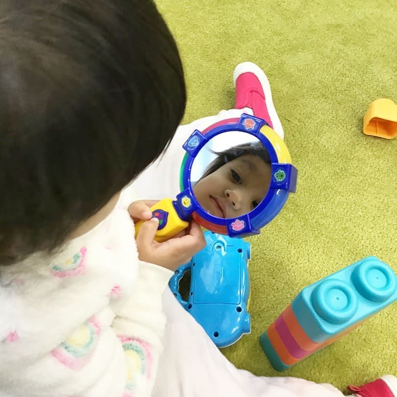 A little girl is looking at her reflection in a toy mirror