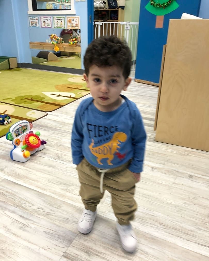 A young boy wearing a blue shirt with a dinosaur on it is standing in a room