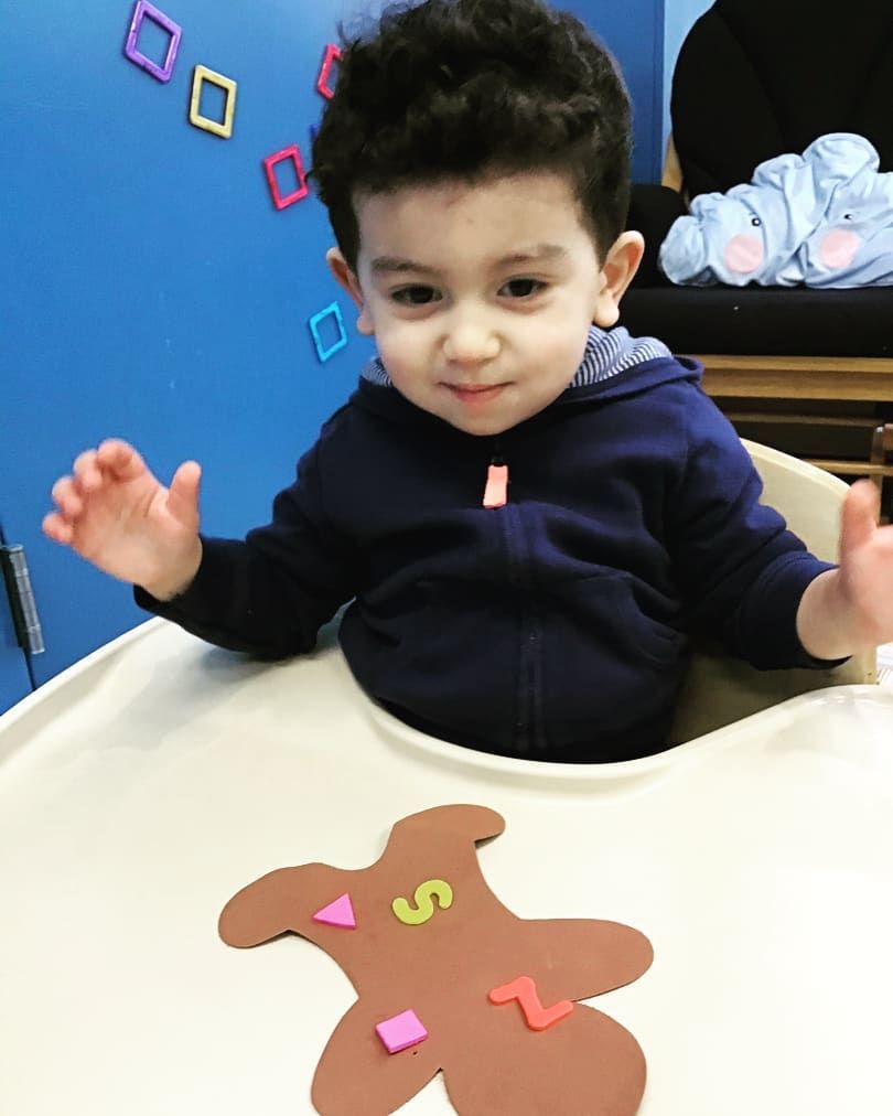 A little boy is sitting in a high chair with a gingerbread bear made out of numbers 5 and 2