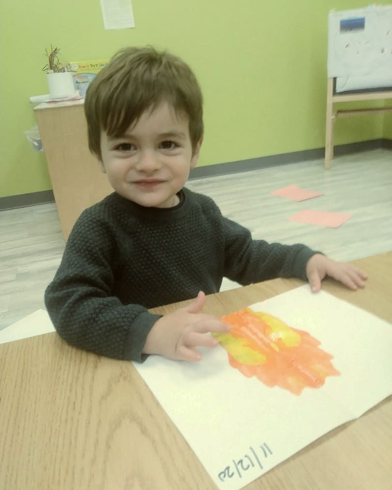 A young boy sits at a table with a drawing of a leaf on it