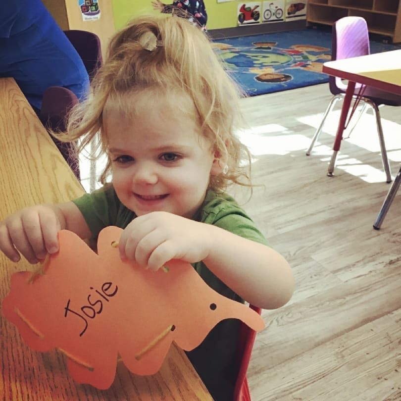 A little girl is holding an orange elephant with the name josie written on it