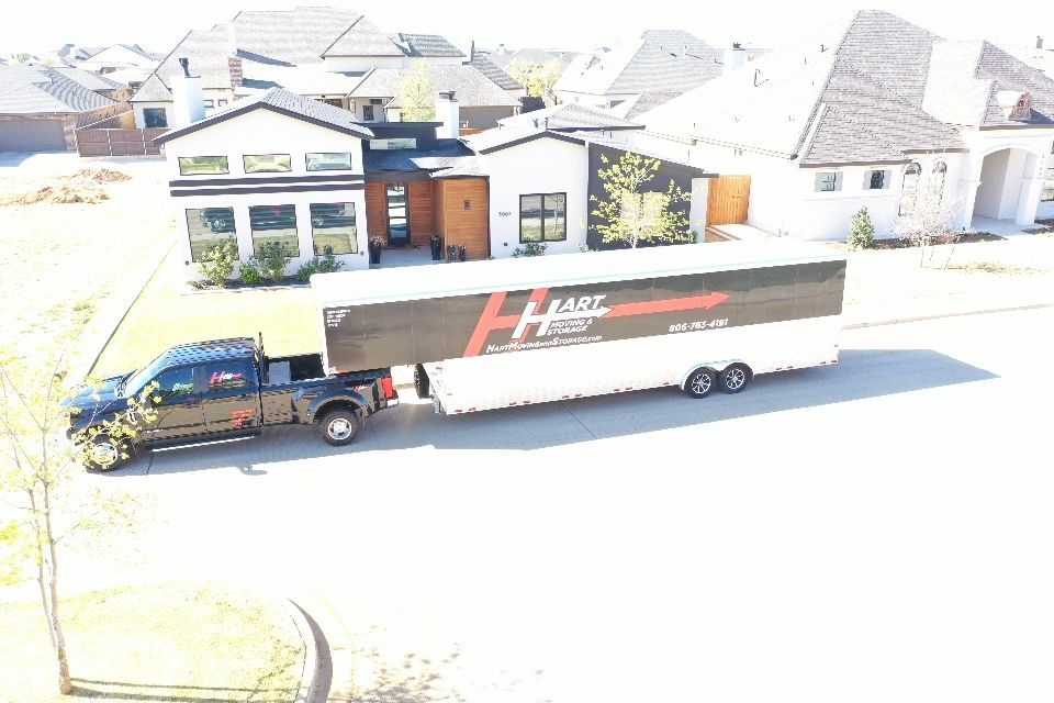Truck pulling a large trailer with a moving company logo in front of a house in a suburban neighborhood.