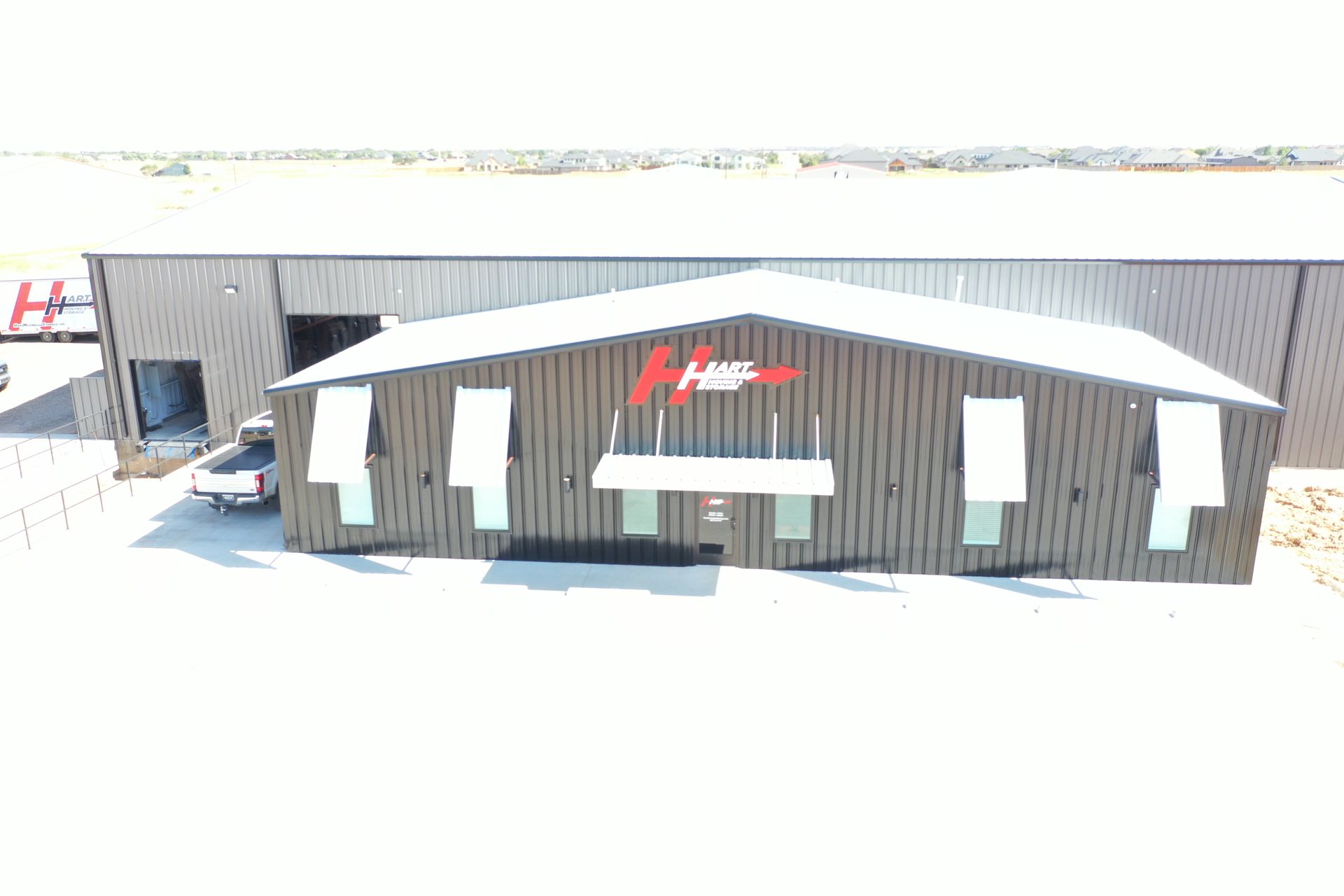 A gray industrial building with a red logo above the entrance and white garage door.