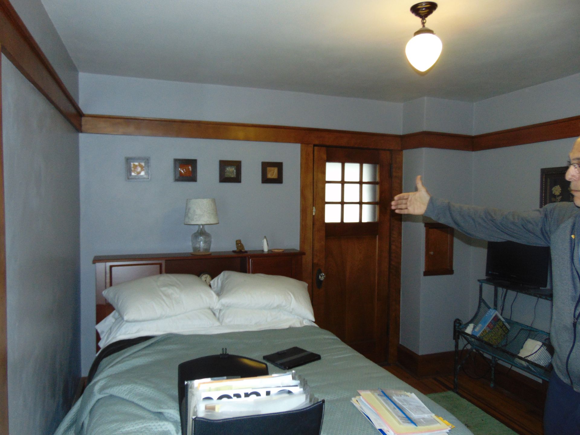 A man giving a thumbs up in a bedroom with a bed
