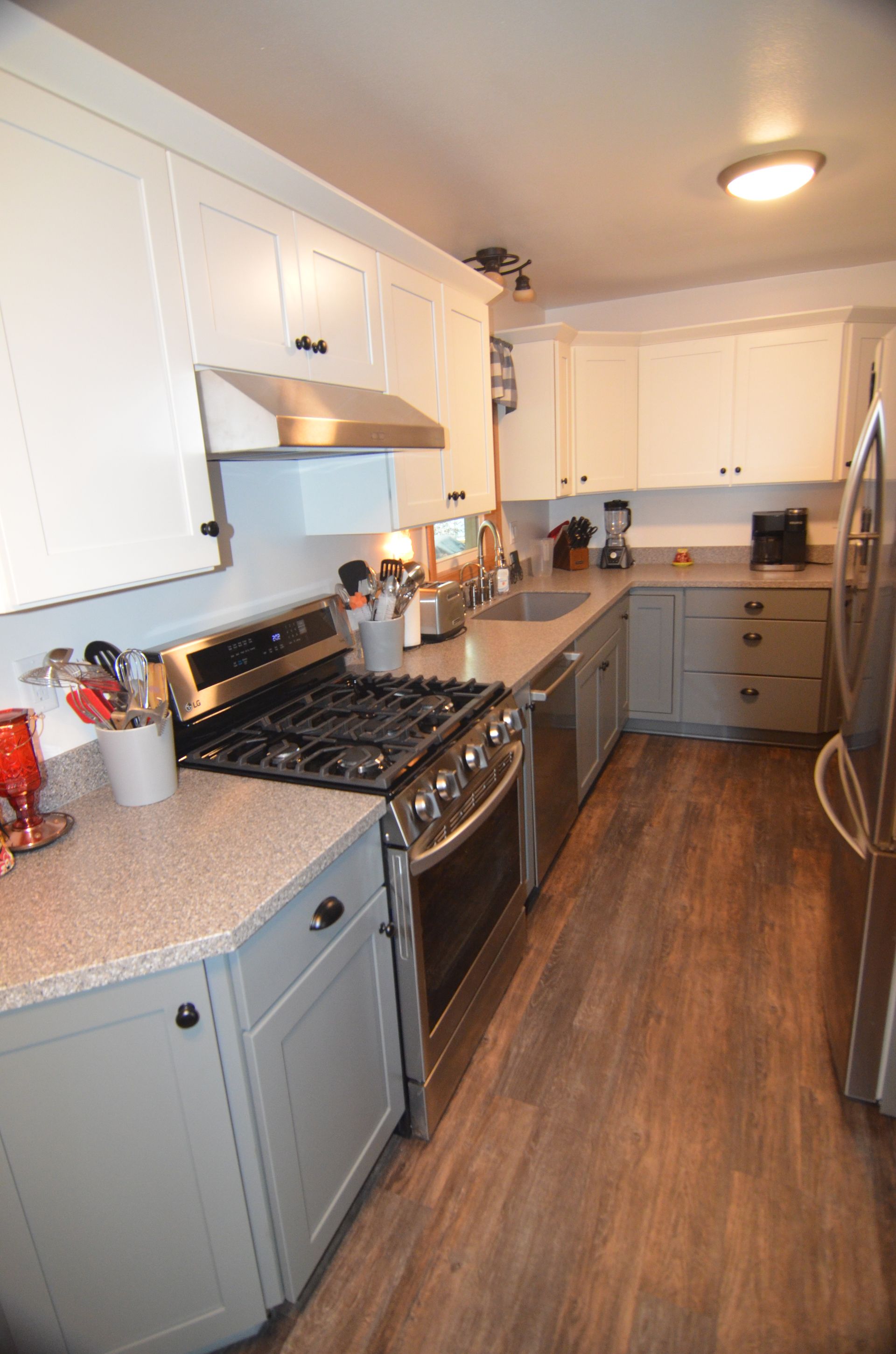 Gray and white kitchen with stainless steel appliances, grey lower cabinets, and wood-look flooring.