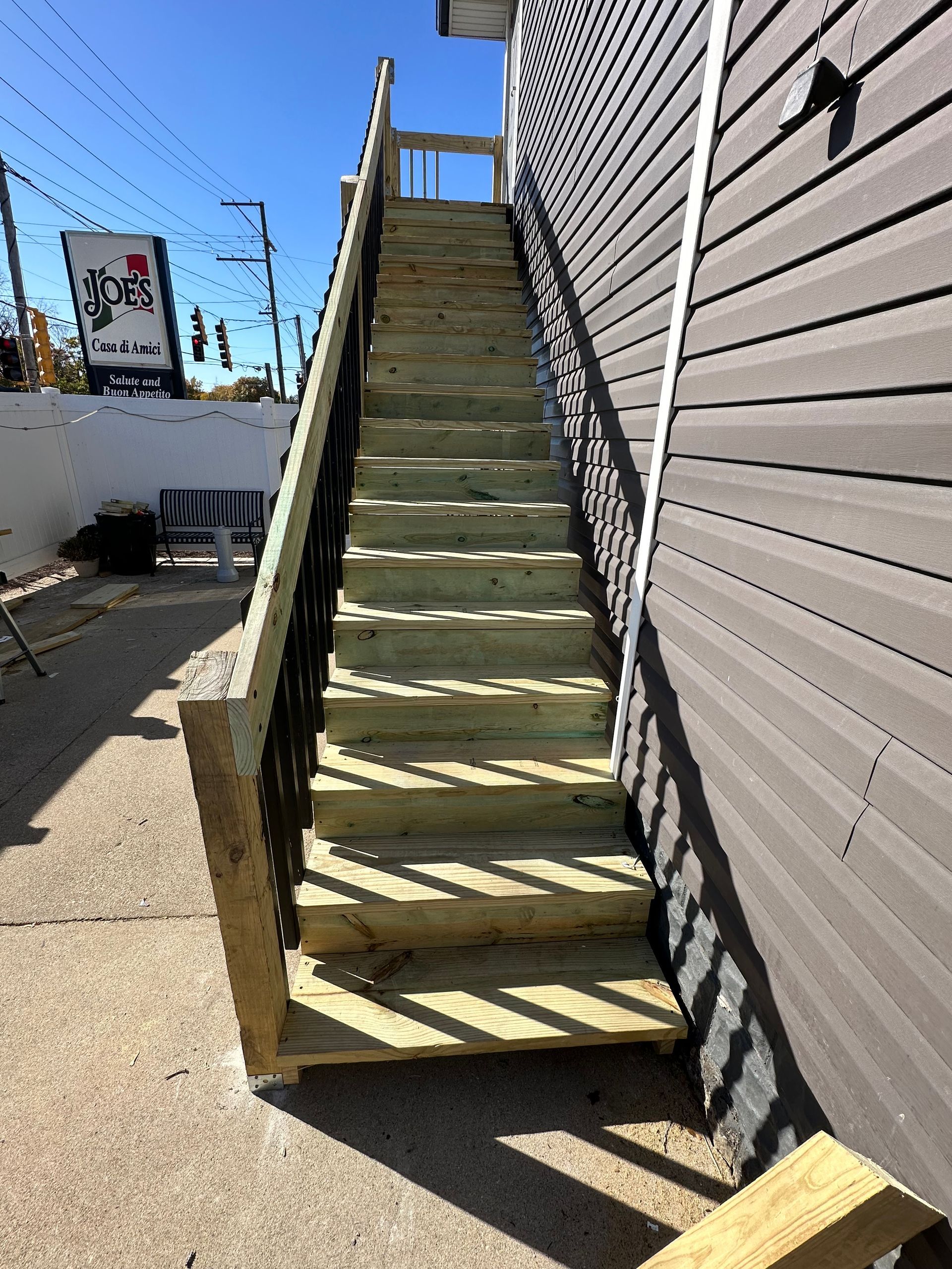 Wooden outdoor staircase with black metal railings leading up to a building with gray siding.