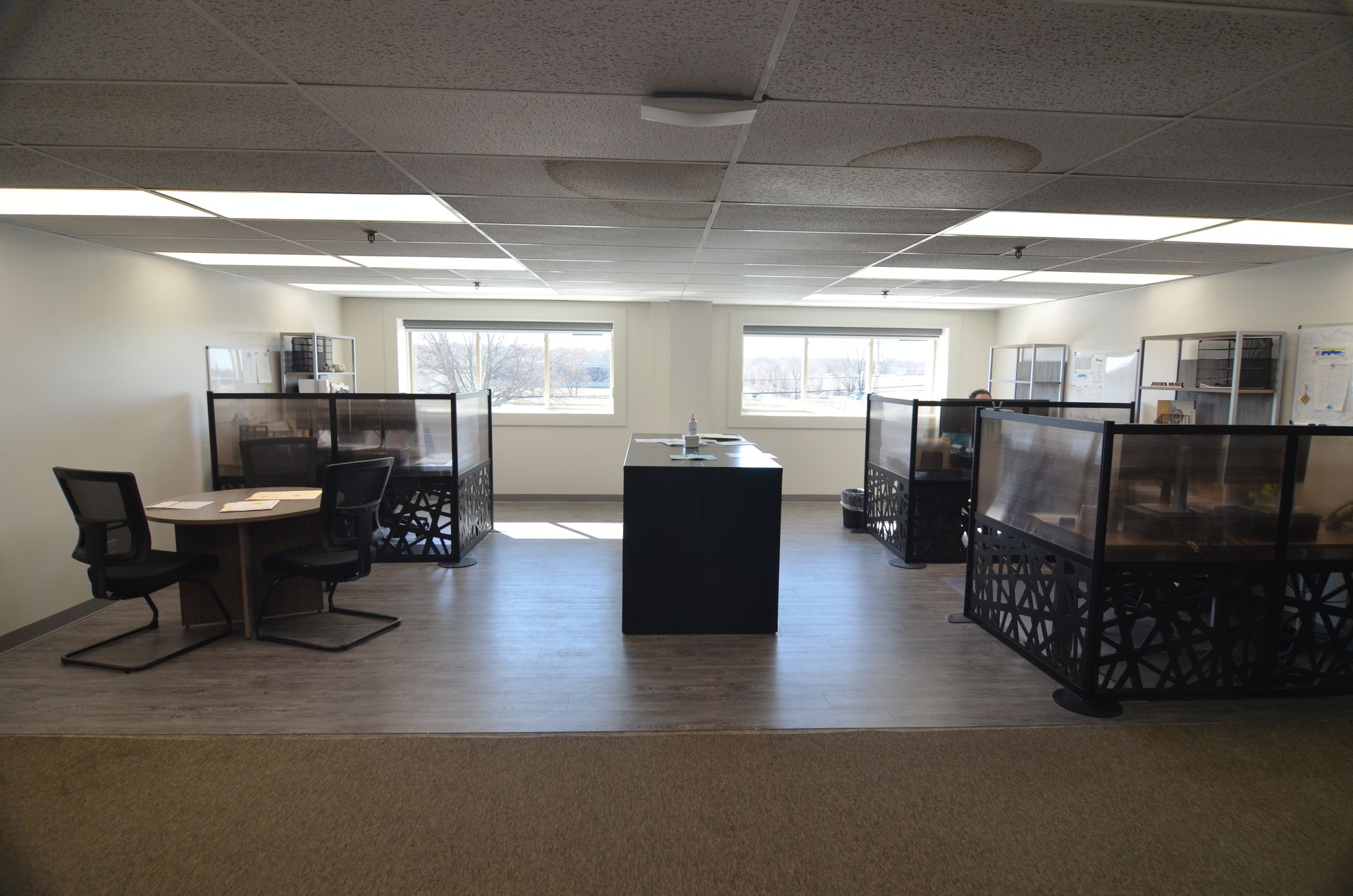 An empty office interior with workstations, windows, and a central black island.