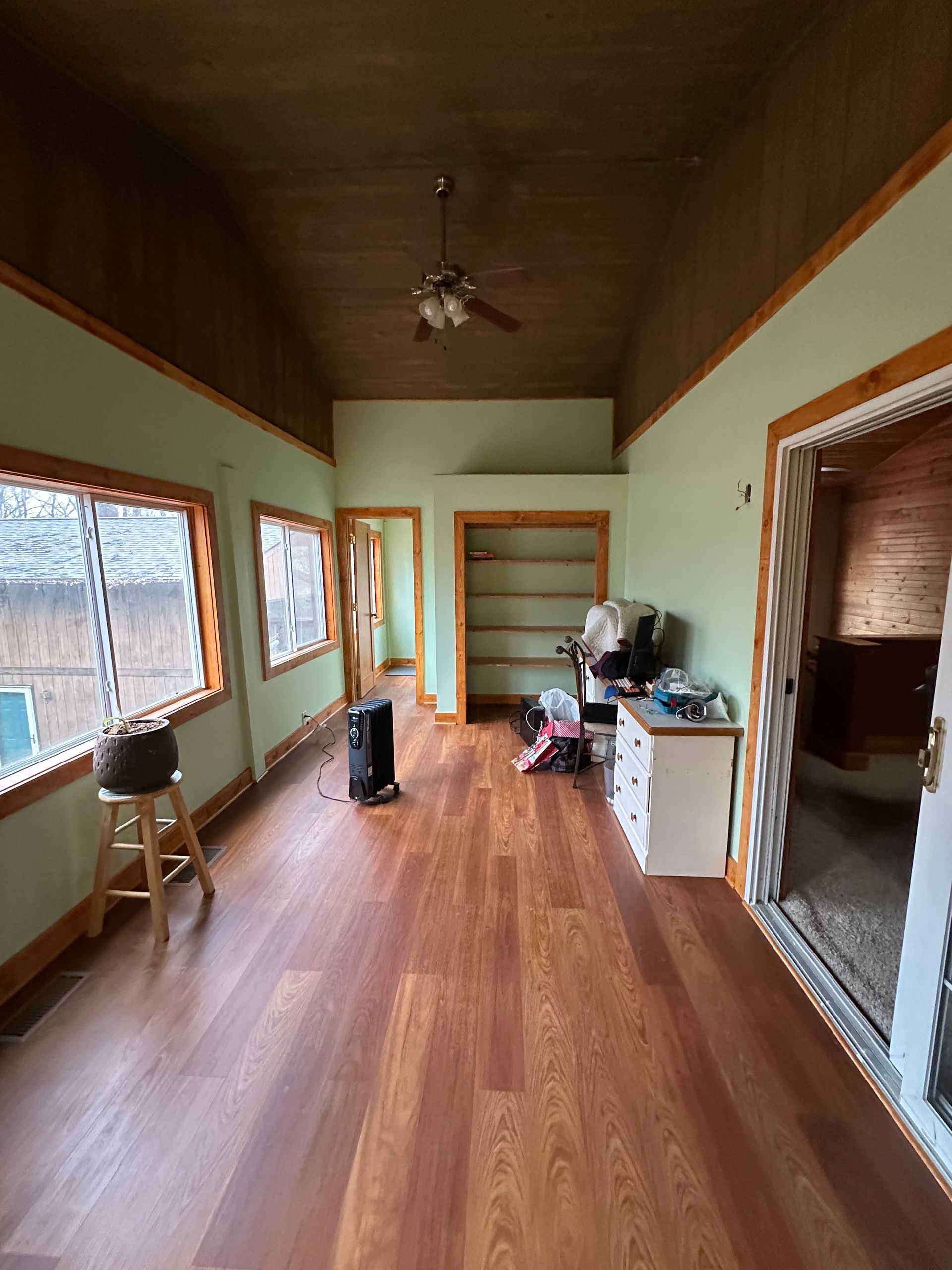 Long room with wood floors and green walls, brown trim. Windows line the left wall, doorway on right.