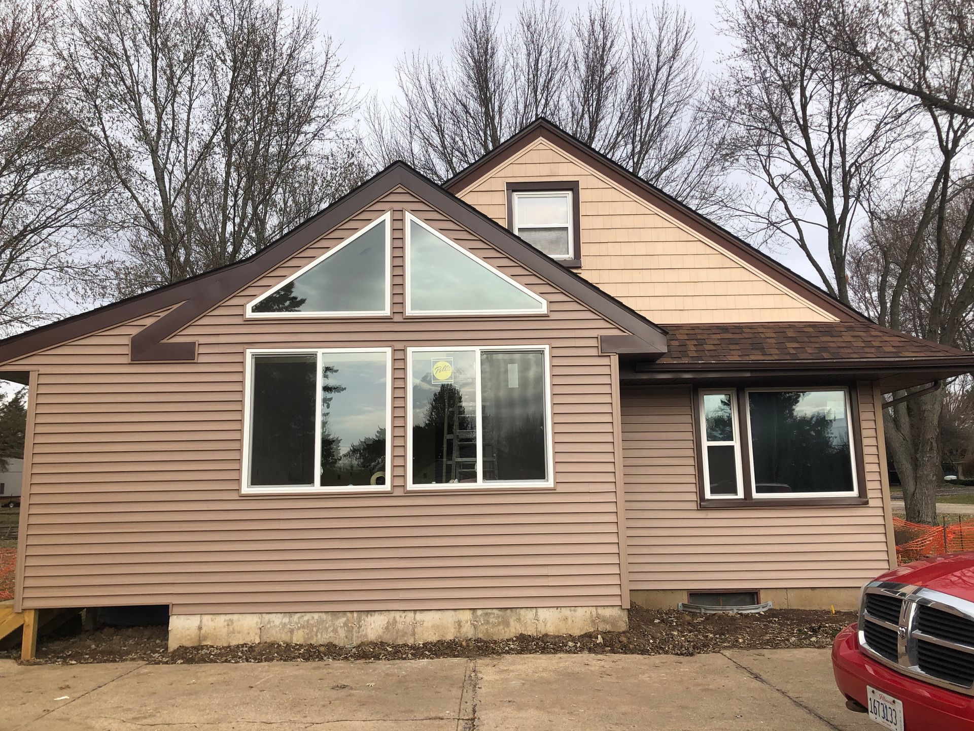 Brown house with triangular and rectangular windows, tan siding, and brown roof.