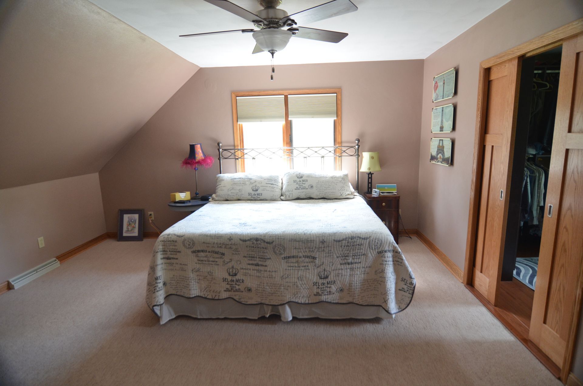 Bedroom with a bed, nightstand, closet, window, and angled ceiling. Walls are mauve, carpet is beige.