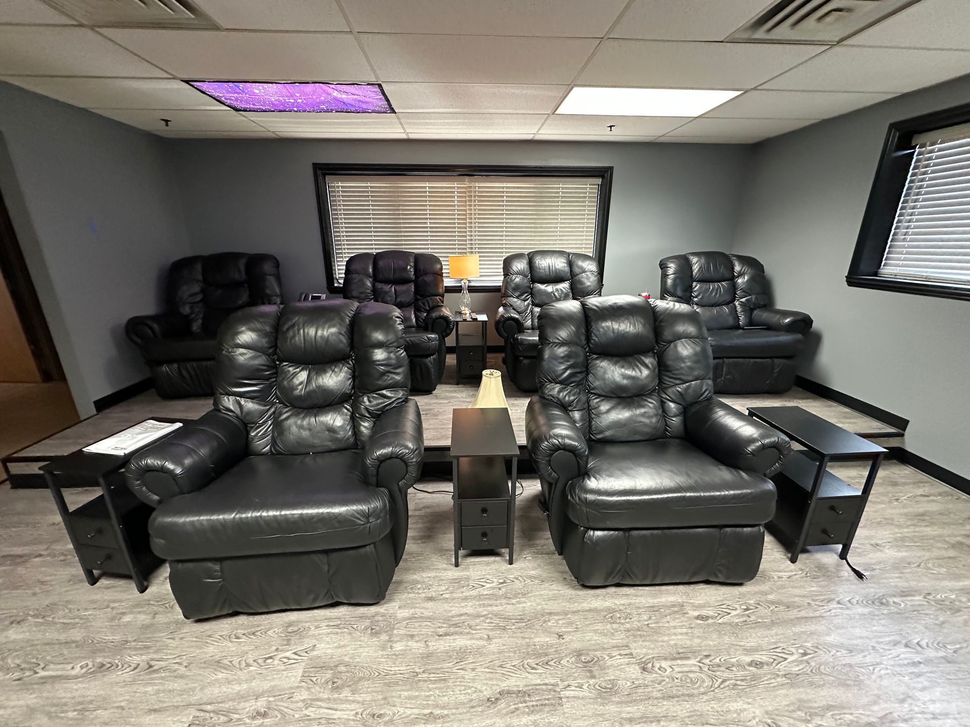 Waiting room with six black leather armchairs and side tables against gray walls.