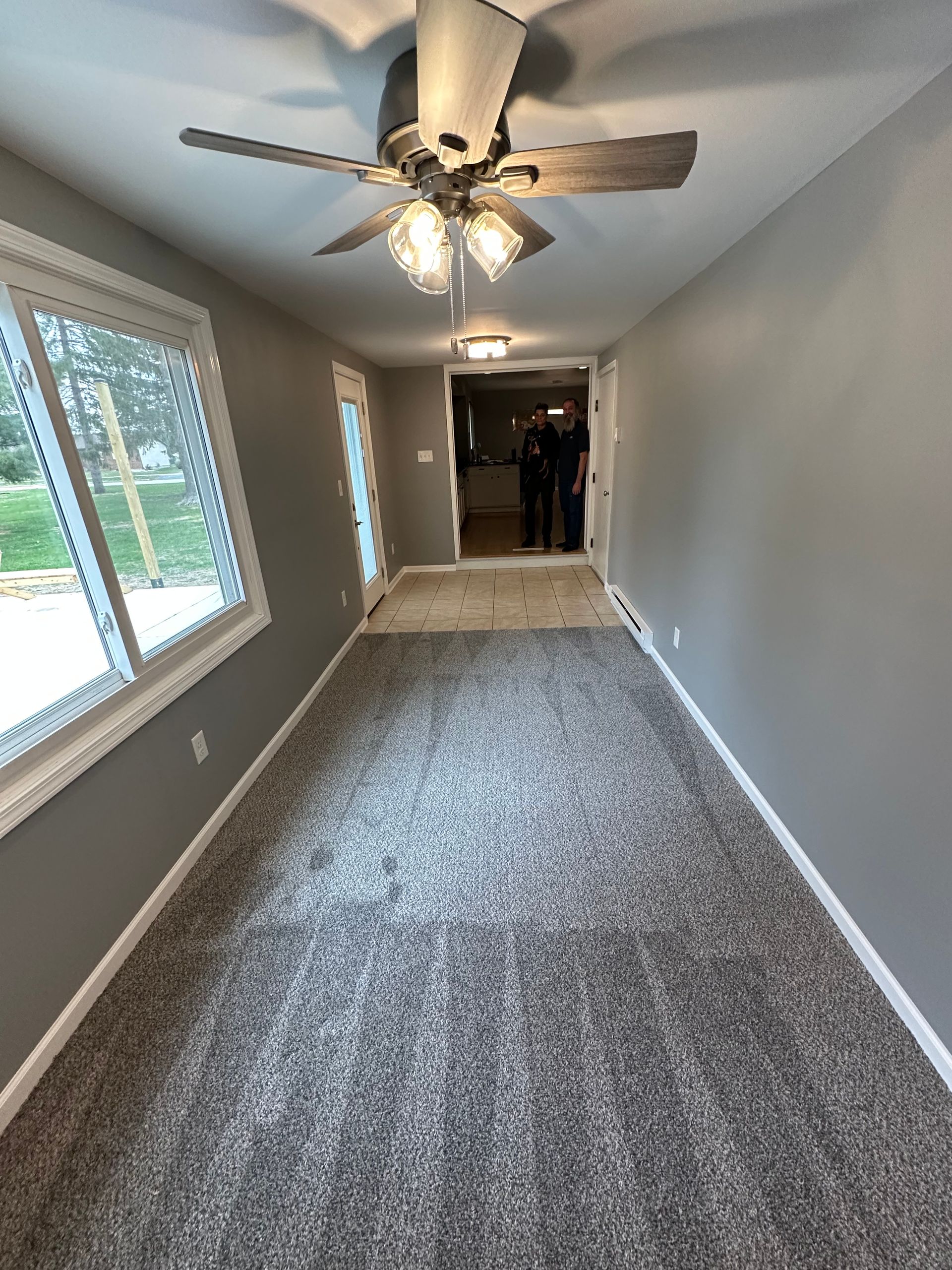 Long, narrow room with gray walls, beige carpet, and a ceiling fan.