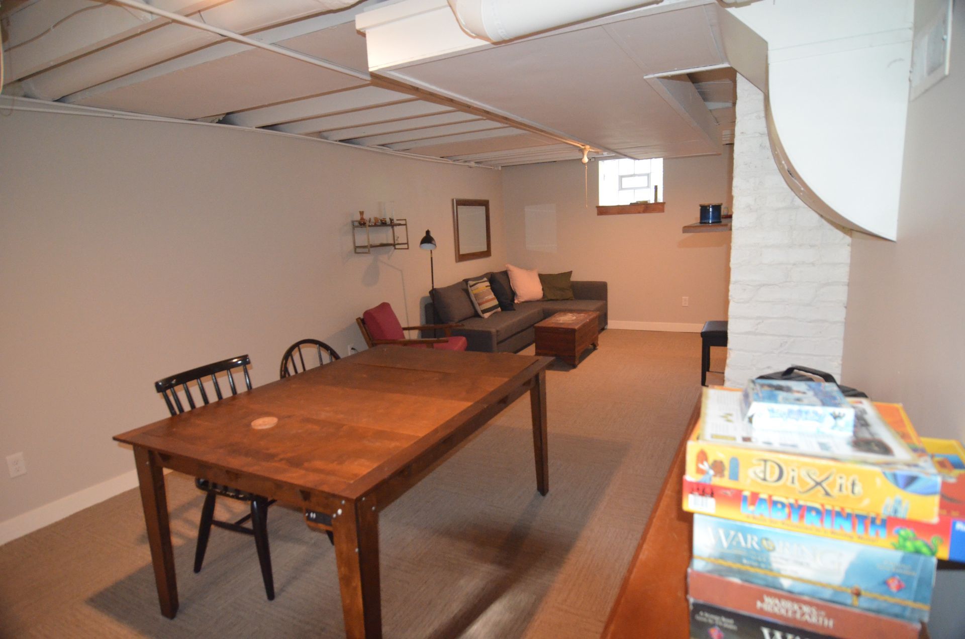 Basement living room with table, sofa, and board games on a shelf.