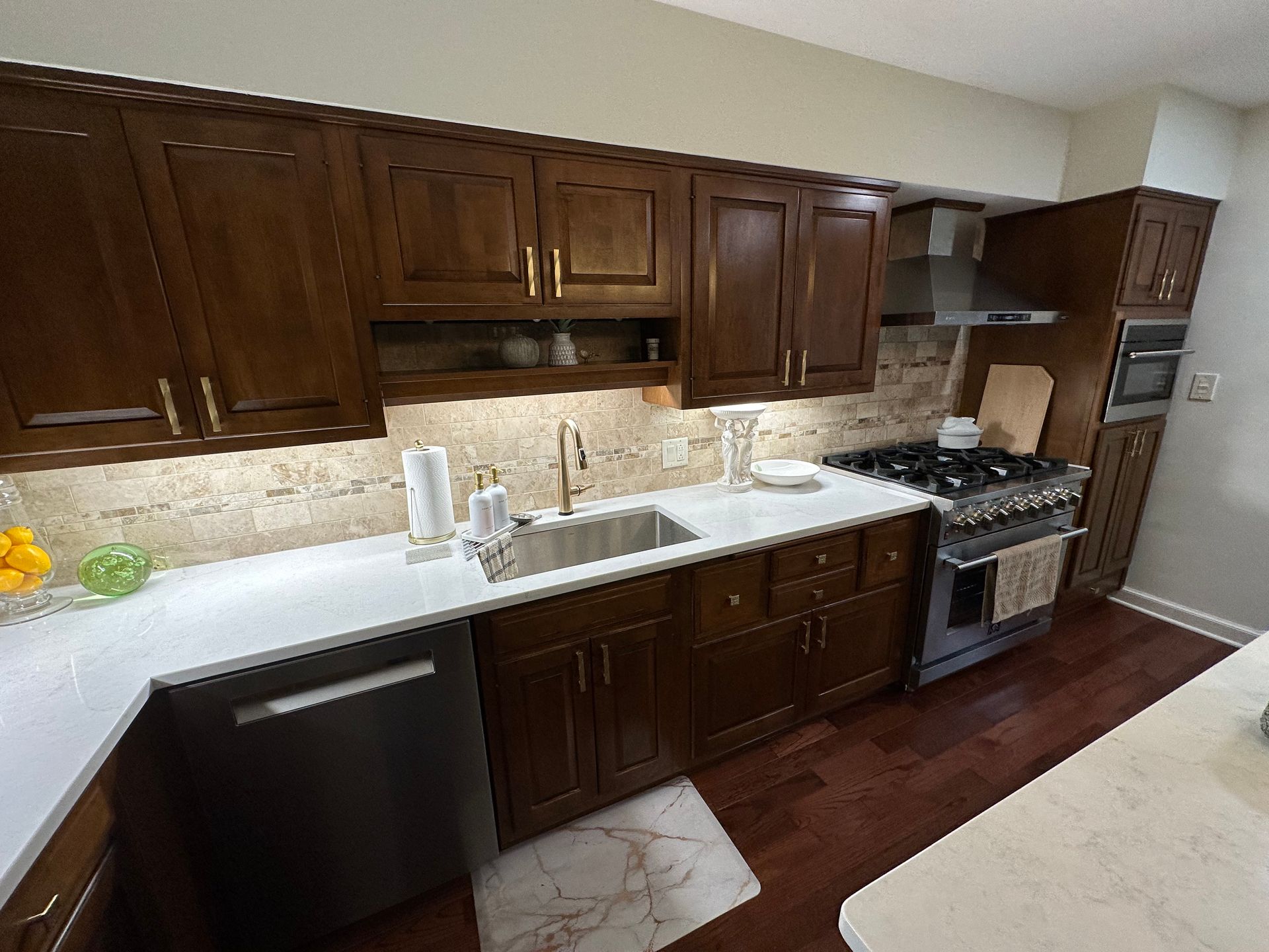 Dark wood kitchen with white countertops, stainless steel appliances, and beige backsplash.