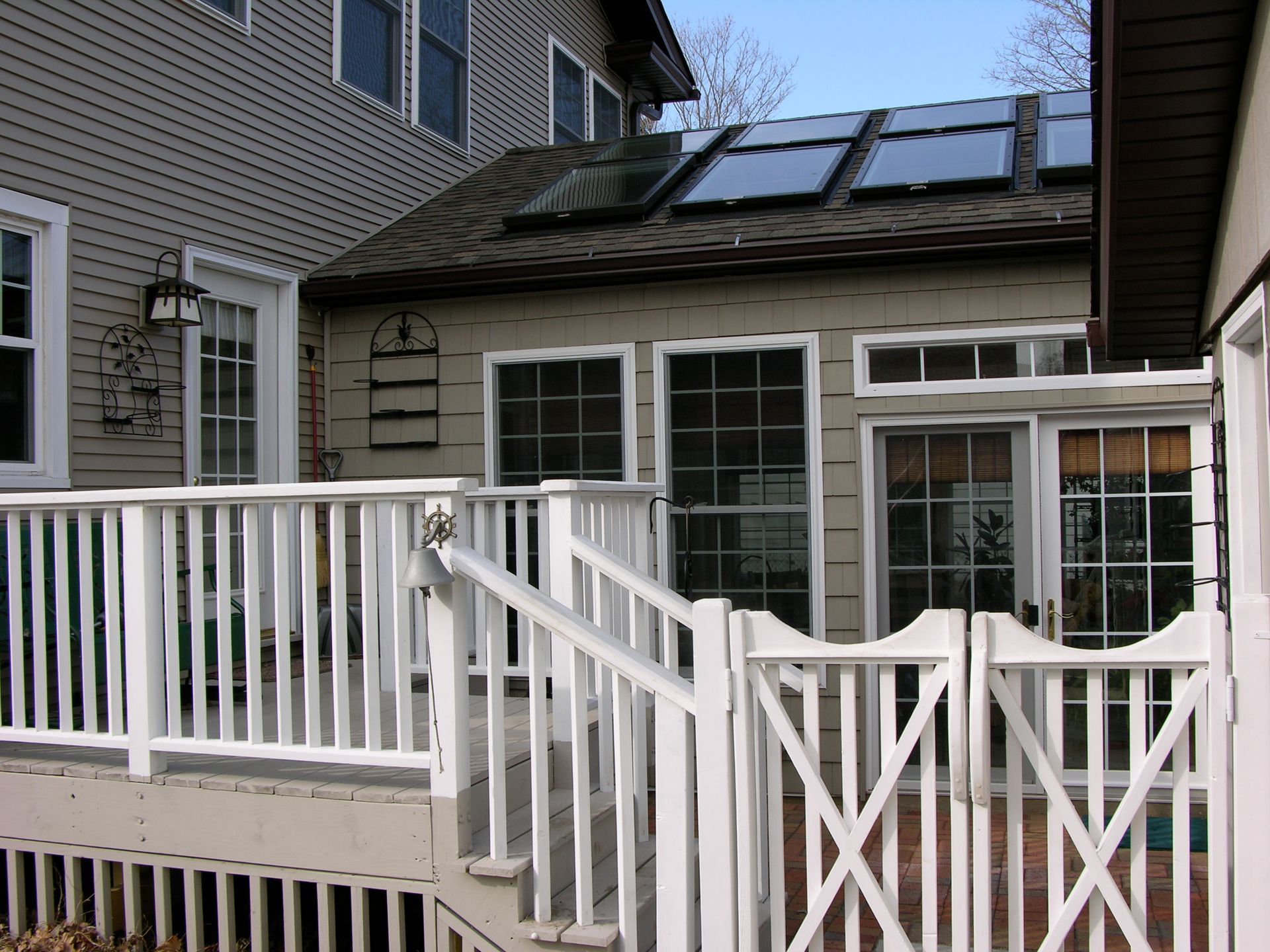 White deck with gate leading to sunroom, tan house exterior, solar panels on roof.