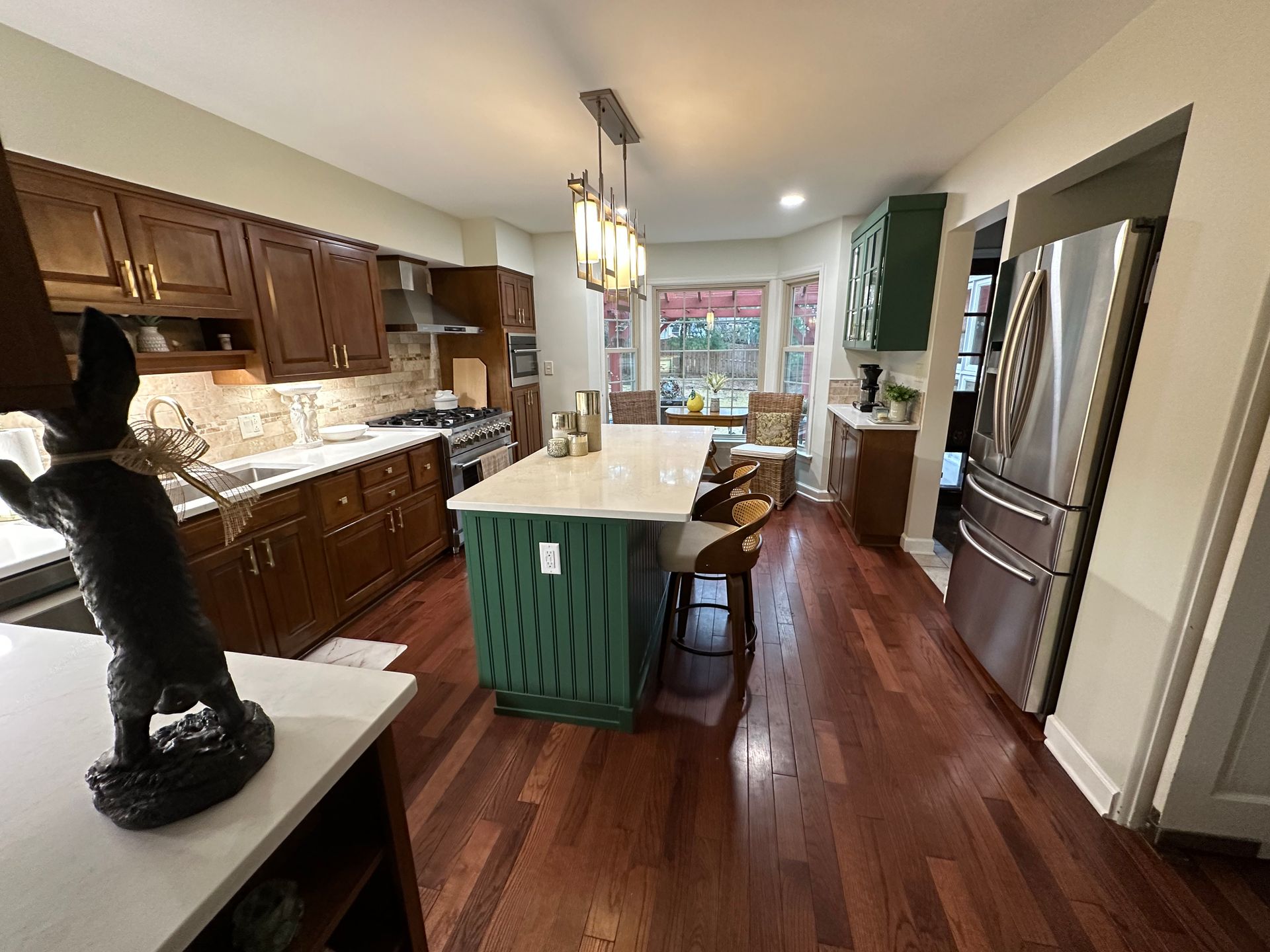 Kitchen with wooden cabinets, green island, stainless steel refrigerator, and hardwood floors.