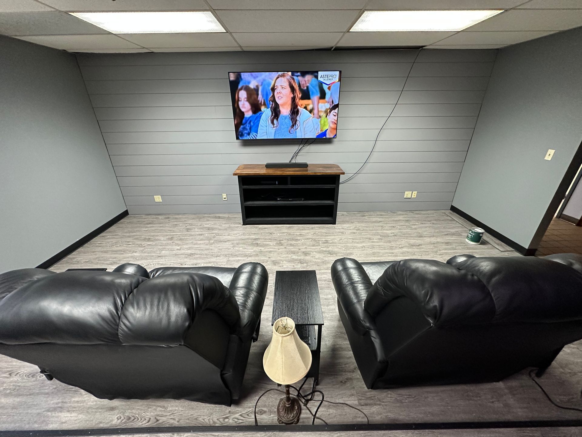 Cozy room with TV, two black recliners, small table, and a cabinet against a gray sloped wall.